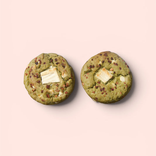 Two green cookies with white chocolate chips on a light pink background
